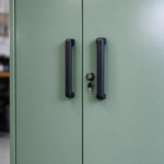 Black cabinet handle and key lock on sage green steel